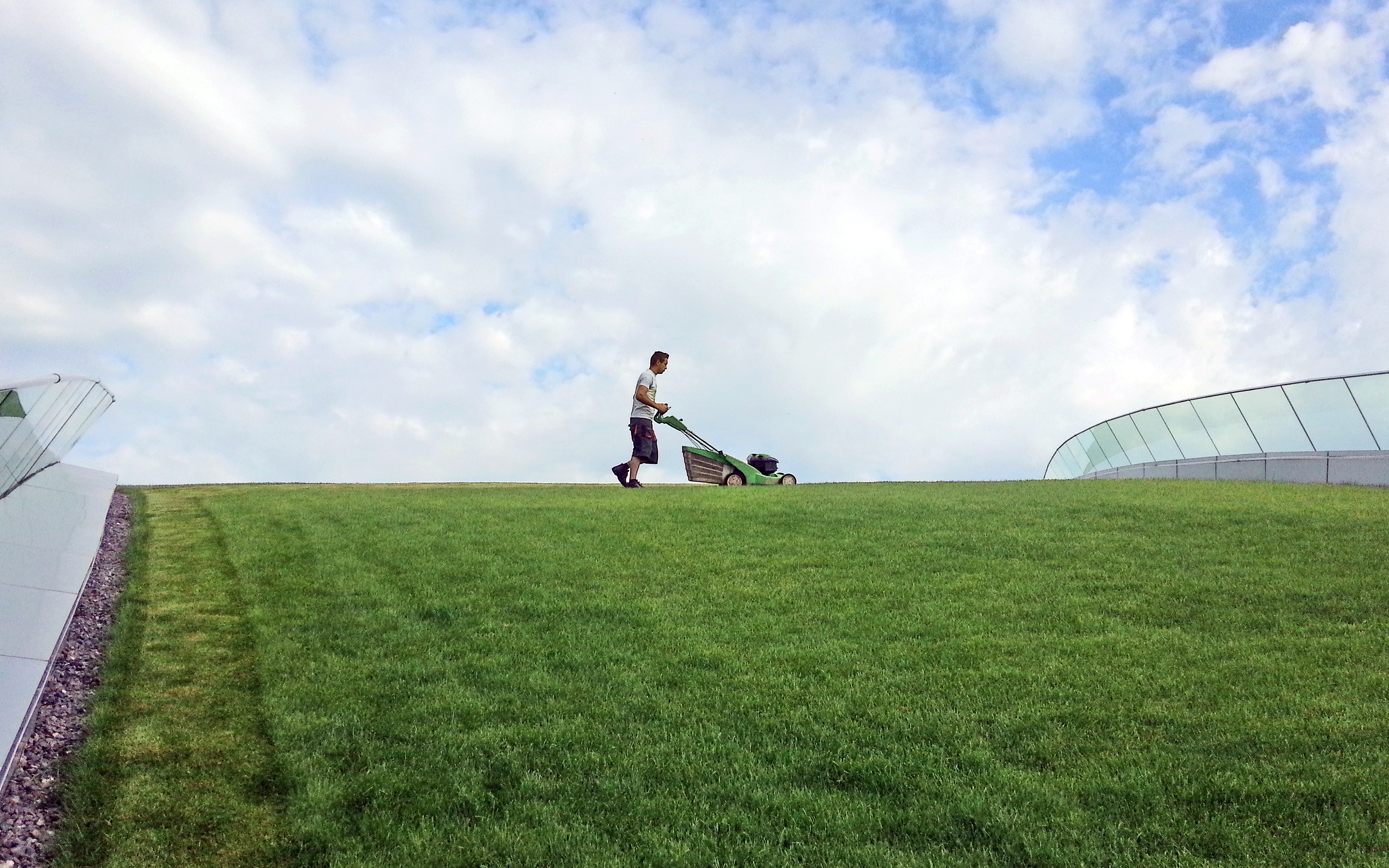 The green roof with its walkable lawn requires intensive maintenance. Man mowing grass on a green roof with lawn